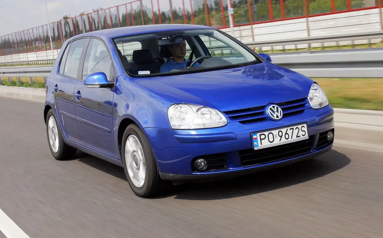 Niebieski Golf 5 z 2004 roku jedzie po drodze. Kierowca w niebieskiej koszulce prowadzi auto.