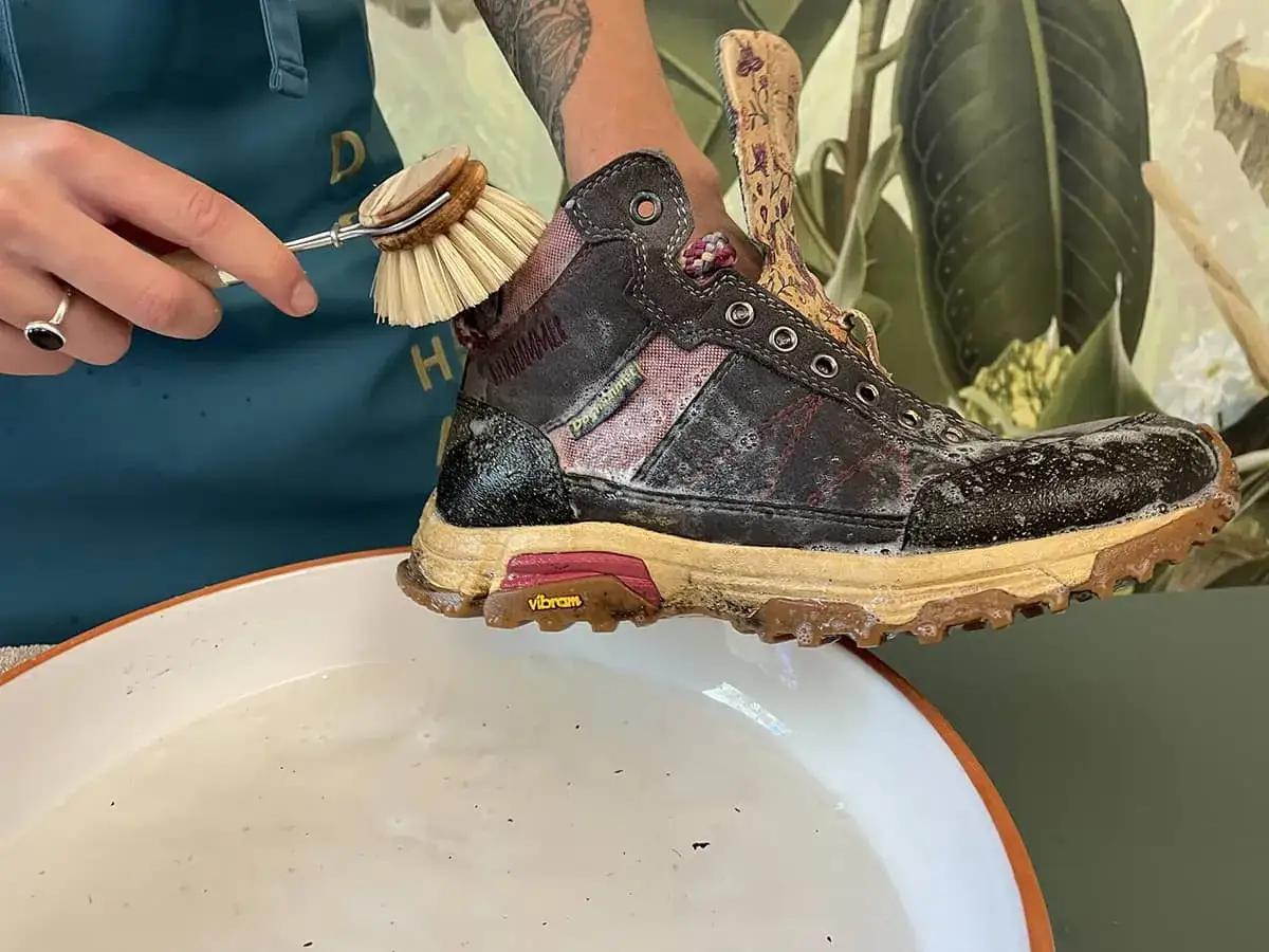 Schuhb&uuml;rste reinigt schmutzige Wanderschuhe in Seifenwasser. So pflegt man Wanderschuhe richtig.