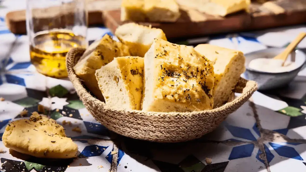 Frisch gebackene Focaccia-Stücke mit Kräutern in einem Korb, daneben Olivenöl. Ein einfaches Focaccia Rezept zum Genießen.