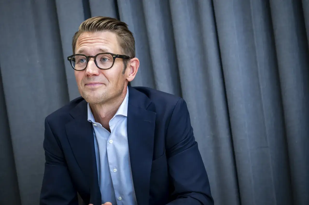 Clas Ohlson VD, med glas&ouml;gon och m&ouml;rkbl&aring; kavaj, sitter framf&ouml;r en gr&aring; rid&aring;.