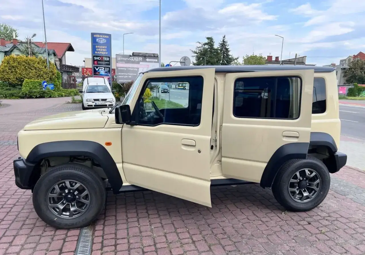 Beżowy Suzuki Jimny 5-drzwiowy z otwartymi drzwiami. Sprawdź suzuki jimny 5-drzwiowy cena i możliwości tego terenowego auta.