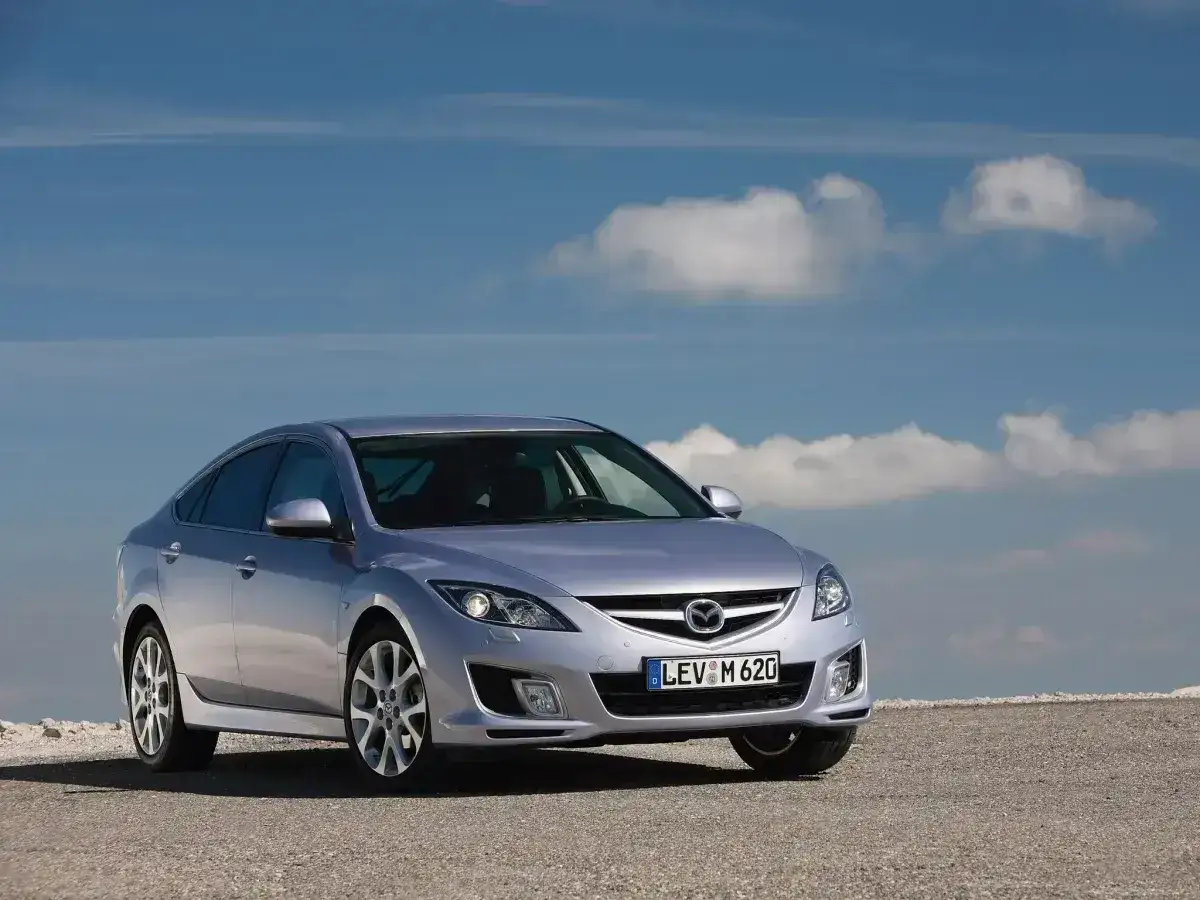 Srebrna Mazda 6 2.0 benzyna na tle błękitnego nieba z chmurami. Elegancka sylwetka samochodu na kamienistym podłożu.