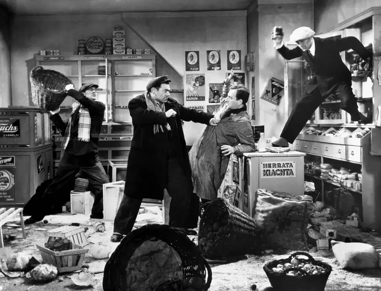 Scena z filmu Michała Waszyńskiego: bójka w sklepie, mężczyźni walczą, jeden rzuca koszem, inny podnosi szklankę.