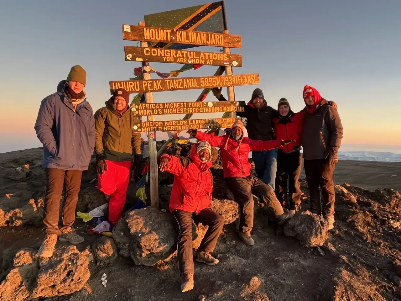 Grupa zdobywc&oacute;w na szczycie Uhuru Peak, najwyższym punkcie Afryki, na tle tablicy z napisem 