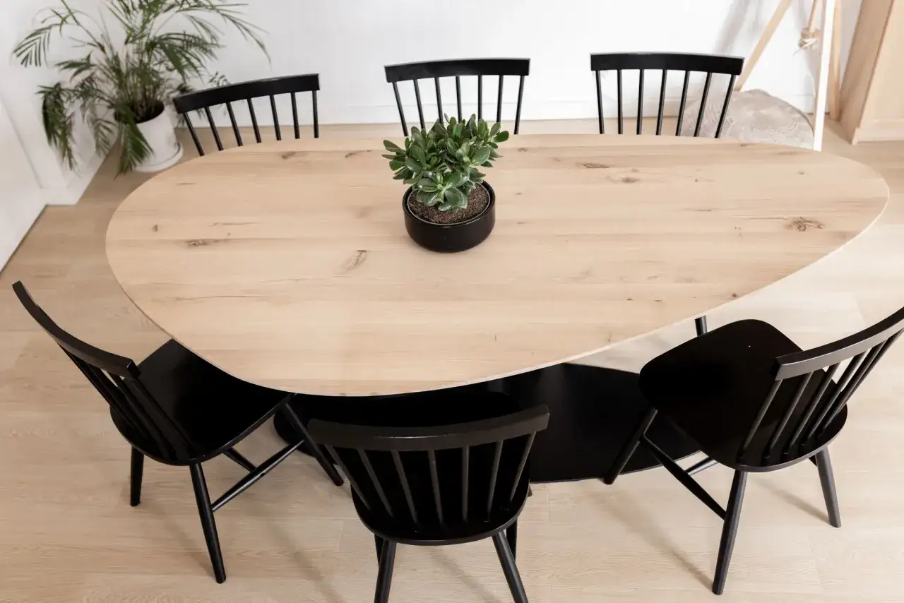 Moderner Esstisch aus hellem Holz mit schwarzen Stühlen und einer grünen Pflanze in der Mitte. Perfekte esstisch inspo für ein stilvolles Zuhause.