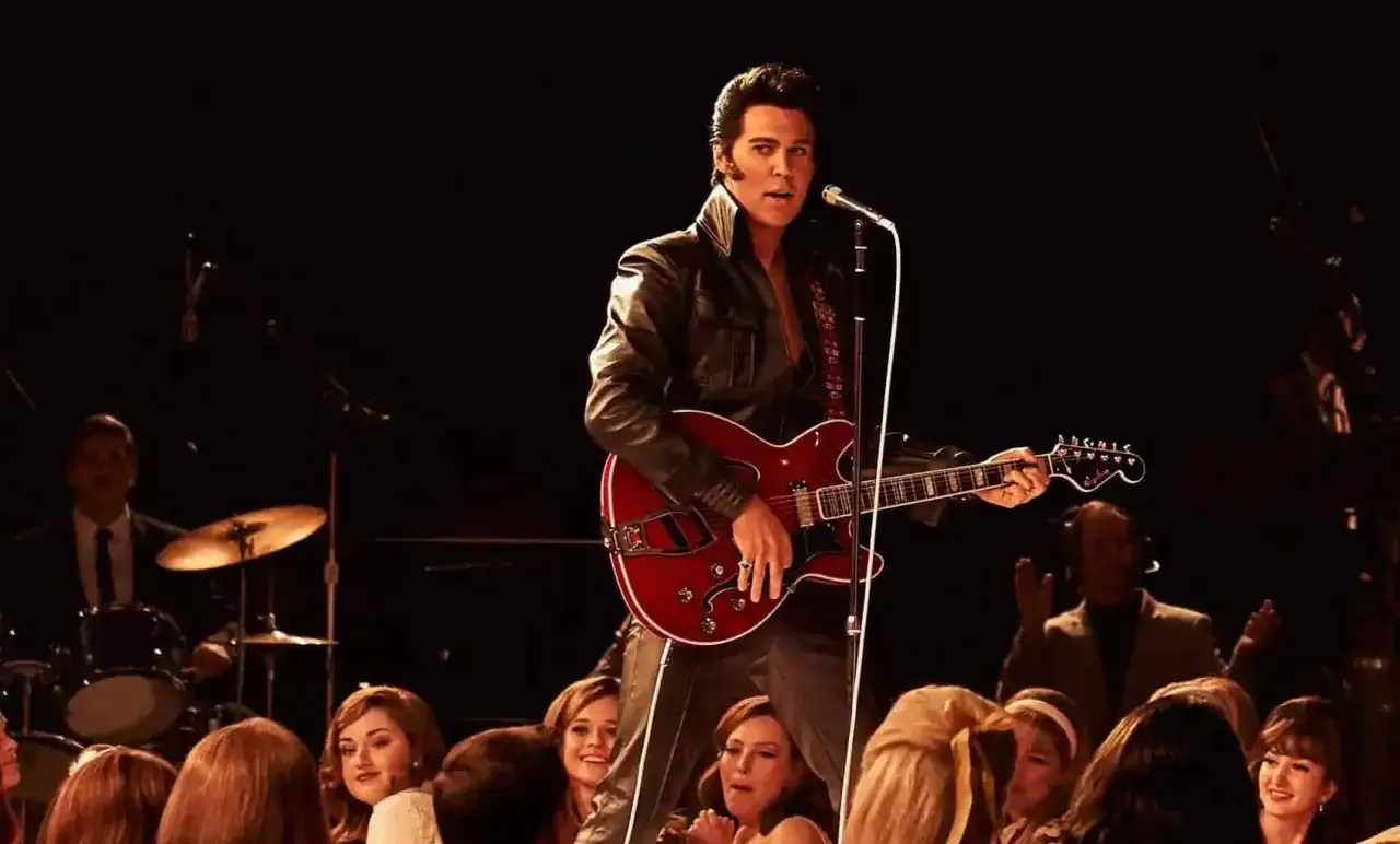 Austin Butler als Elvis Presley in seinem ikonischen Lederoutfit, Gitarre spielend und singend, vor jubelndem Publikum. Ein Moment aus dem Elvis Presley Movie.