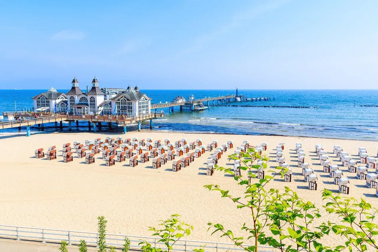 Ein langer Pier mit einem Geb&auml;ude f&uuml;hrt ins Meer. Am Strand stehen viele Strandk&ouml;rbe. Ein sch&ouml;ner Strand in Deutschland.