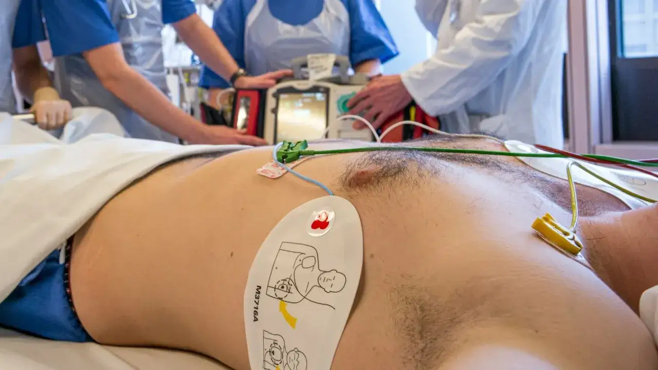 Zespół medyczny przygotowuje się, kiedy defibrylacja jest konieczna. Na klatce piersiowej pacjenta widoczne są elektrody i przewody podłączone do aparatu.