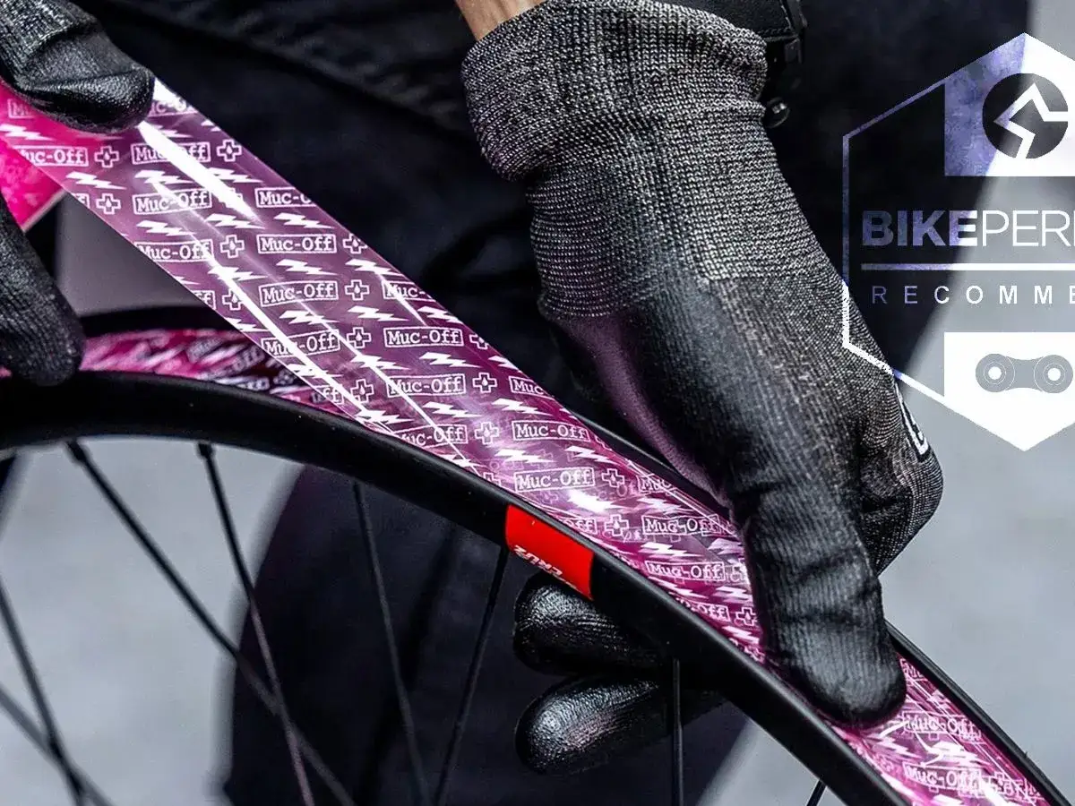 Hands in gloves apply pink tubeless rim tape, showing how to tape tubeless rims for a secure seal.