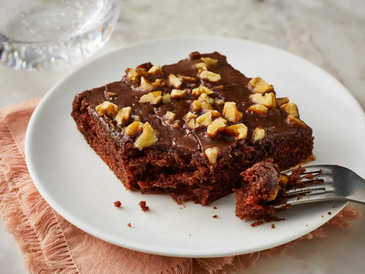 Ein saftiger Schokoladenkuchen mit Nüssen, der zeigt, wie einfach backen sein kann. Ein Stück ist bereits angeschnitten.