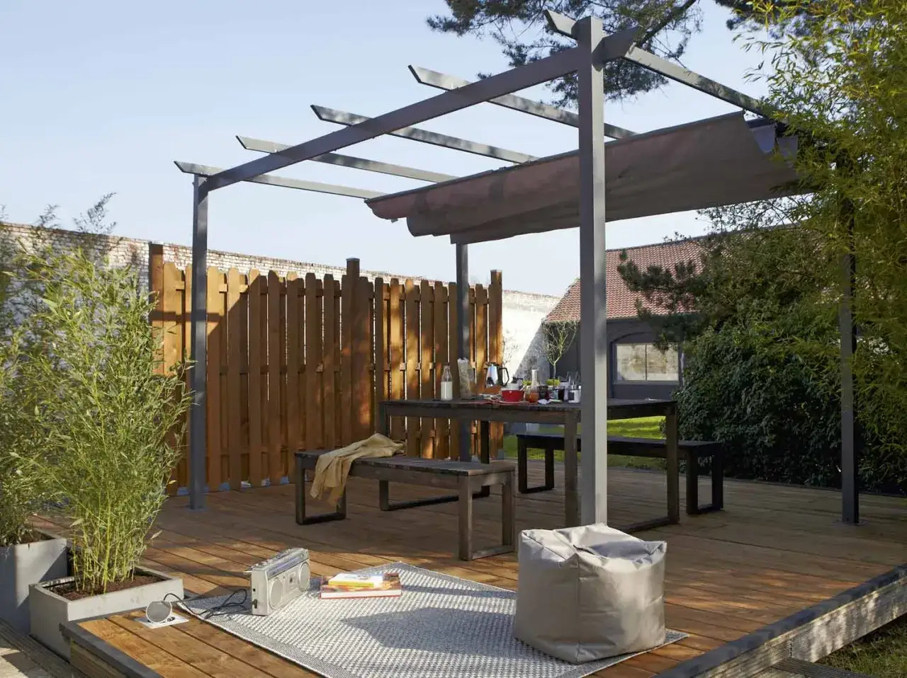 Une tonnelle moderne sur une terrasse en bois, avec table et bancs. Idéal pour savoir comment monter une tonnelle et profiter du jardin.