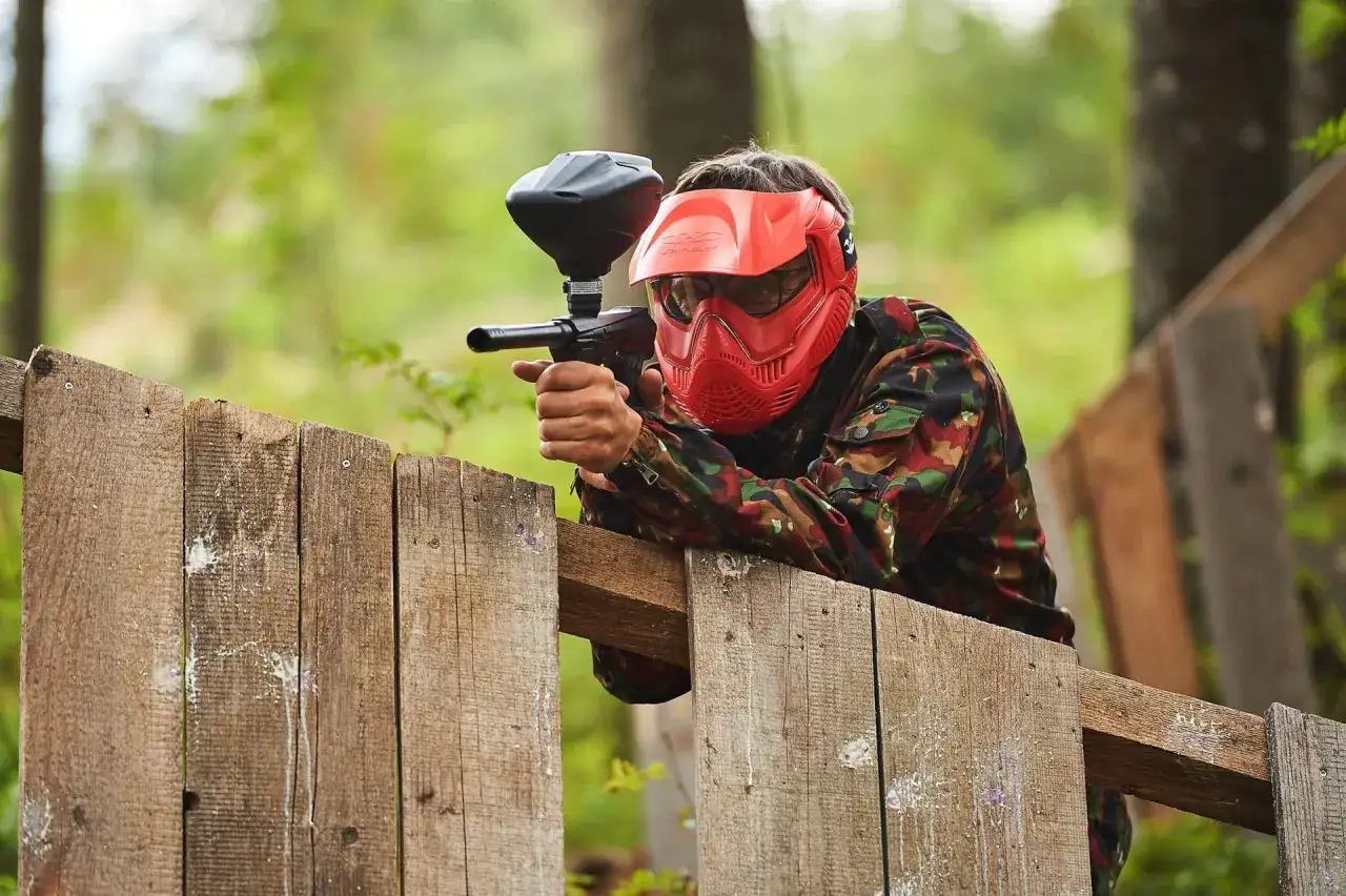 Chłopak w czerwonej masce i moro celuje z markera do paintballa, przygotowując się na ekstremalny wieczór kawalerski.