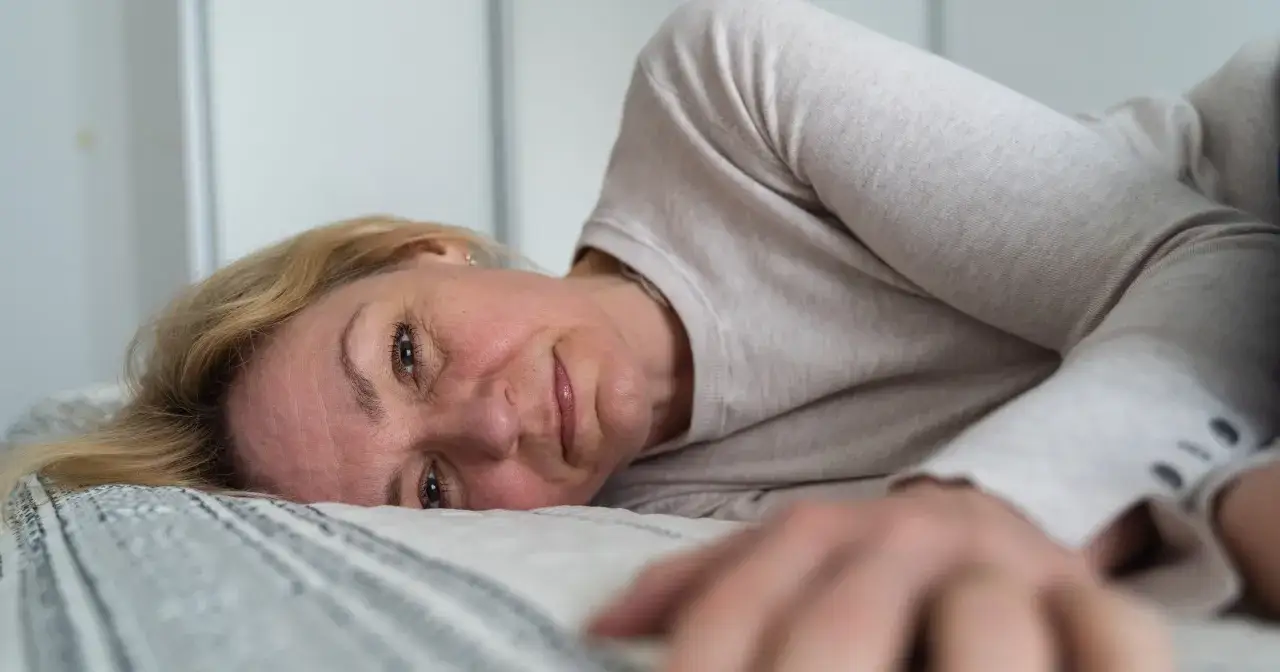 Kobieta leży w łóżku, zamyślona, być może po przebudzeniu z powodu nocnych potów.