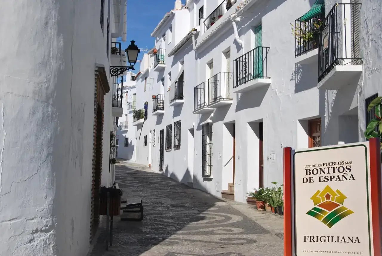 Calle empedrada en Frigiliana, uno de los pueblos más bonitos de España. Casas blancas con balcones de hierro y macetas.