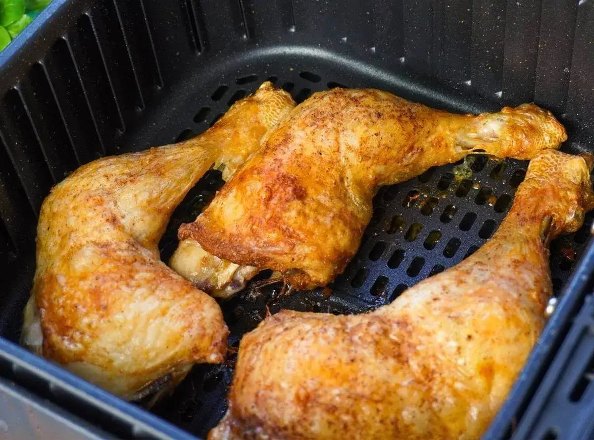 Drei goldbraune Hähnchenschenkel liegen in einem Airfryer-Korb.