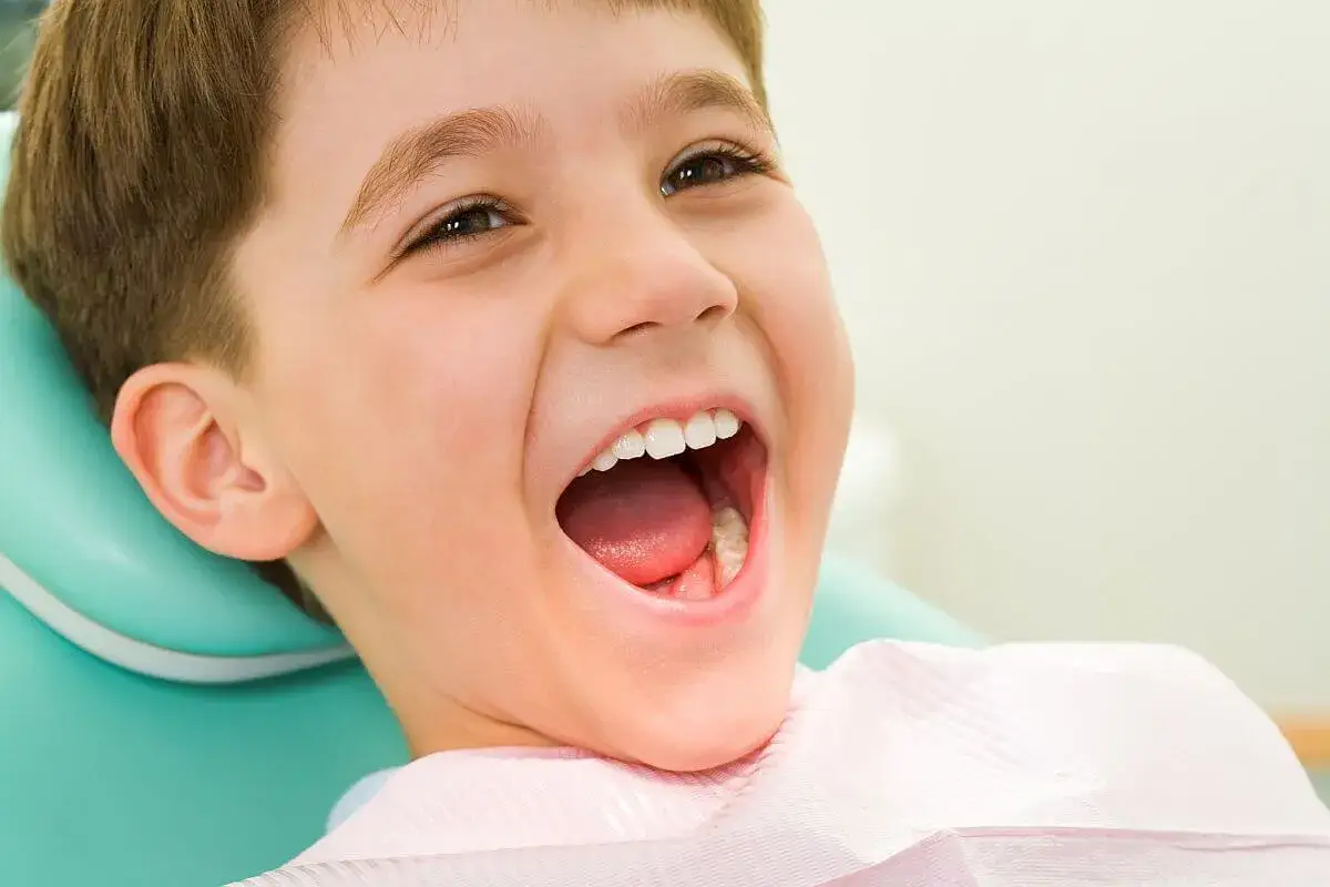 Uśmiechnięty chłopiec pokazuje swoje zdrowe zęby mleczne, siedząc na fotelu dentystycznym.