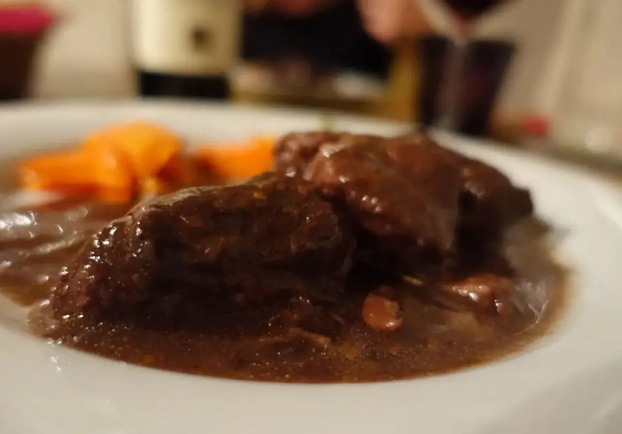 Brasato al Barolo ricetta originale piemontese: succulenti pezzi di carne in salsa scura, accompagnati da carote arancioni.