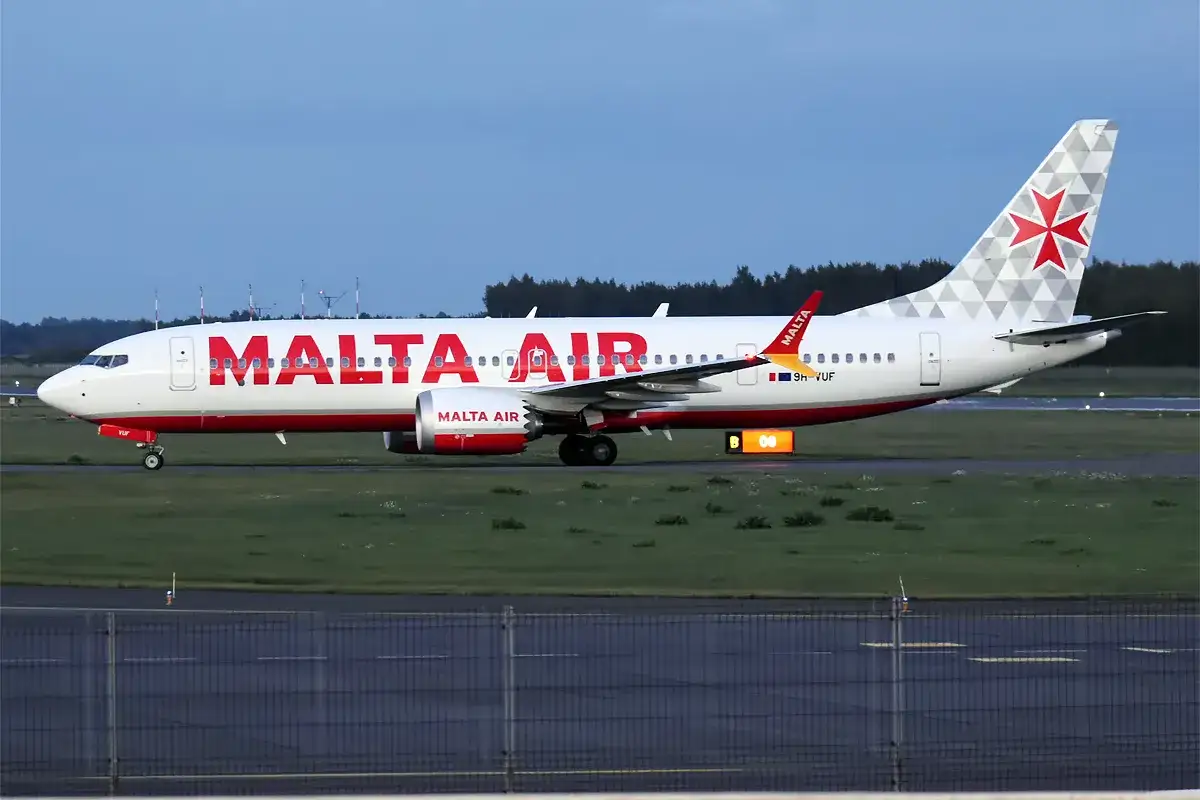 Samolot Malta Air z charakterystycznym czerwonym napisem i krzyżem na ogonie na płycie lotniska.