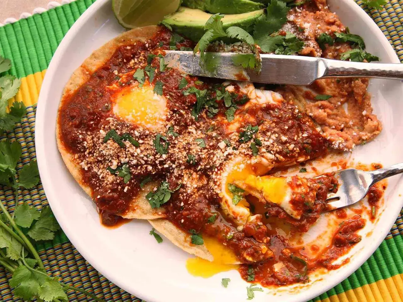 Un plat de huevos rancheros appétissant avec des œufs coulants, de la sauce rouge épicée, des haricots frits, de l'avocat et de la coriandre fraîche.