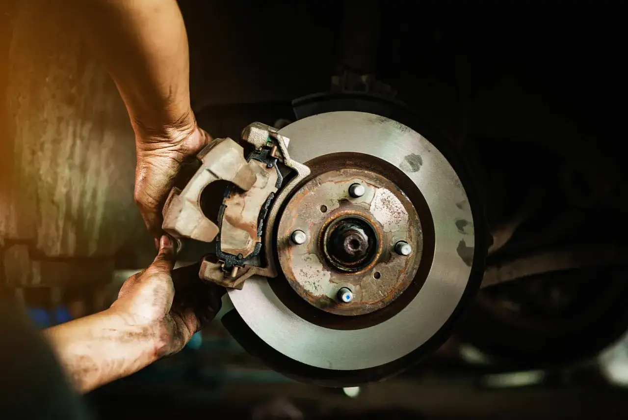 Mechanik sprawdza hamulce, szukając przyczyn zapieczonych tłoczków w zacisku hamulcowym. Widoczny jest element układu hamulcowego z tarczą i zaciskiem.
