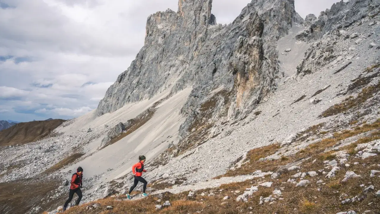 Zwei Läufer im roten und schwarzen Outfit absolvieren ihr trailrunning training auf einem steinigen Bergpfad.