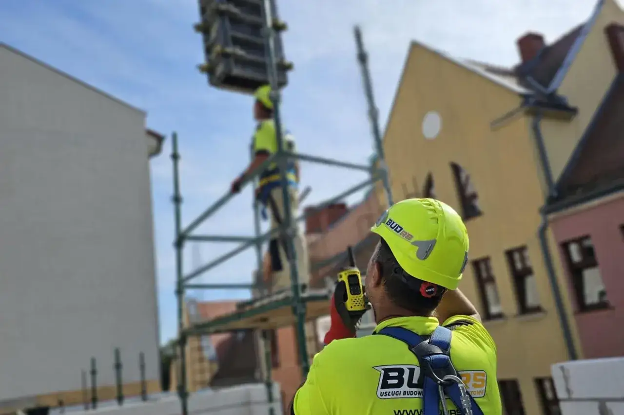 Budowlaniec w żółtym kasku i kamizelce z krótkofalówką na budowie.