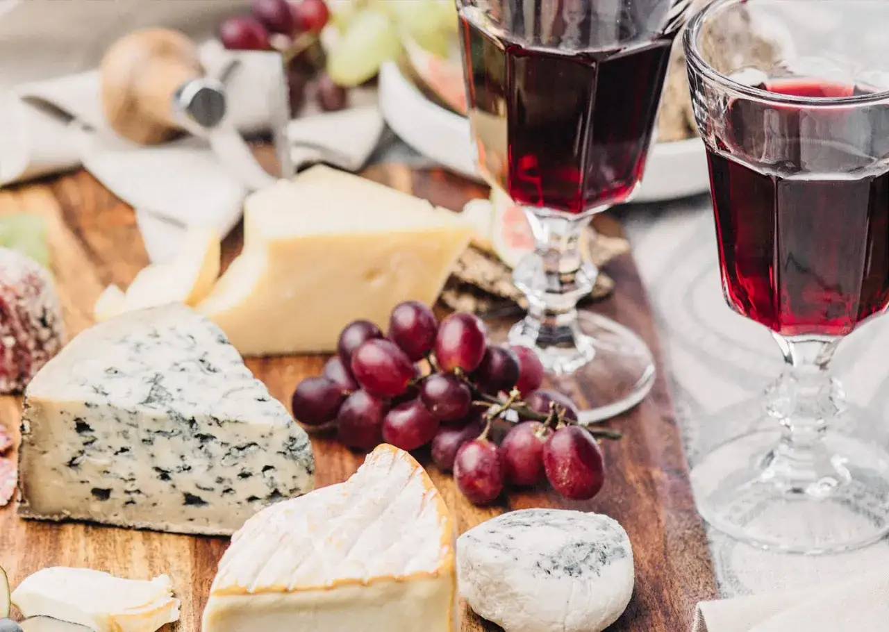 Plateau de fromages vari&eacute;s, dont un fromage de l'abbaye de C&icirc;teaux, avec des raisins et deux verres de vin rouge.