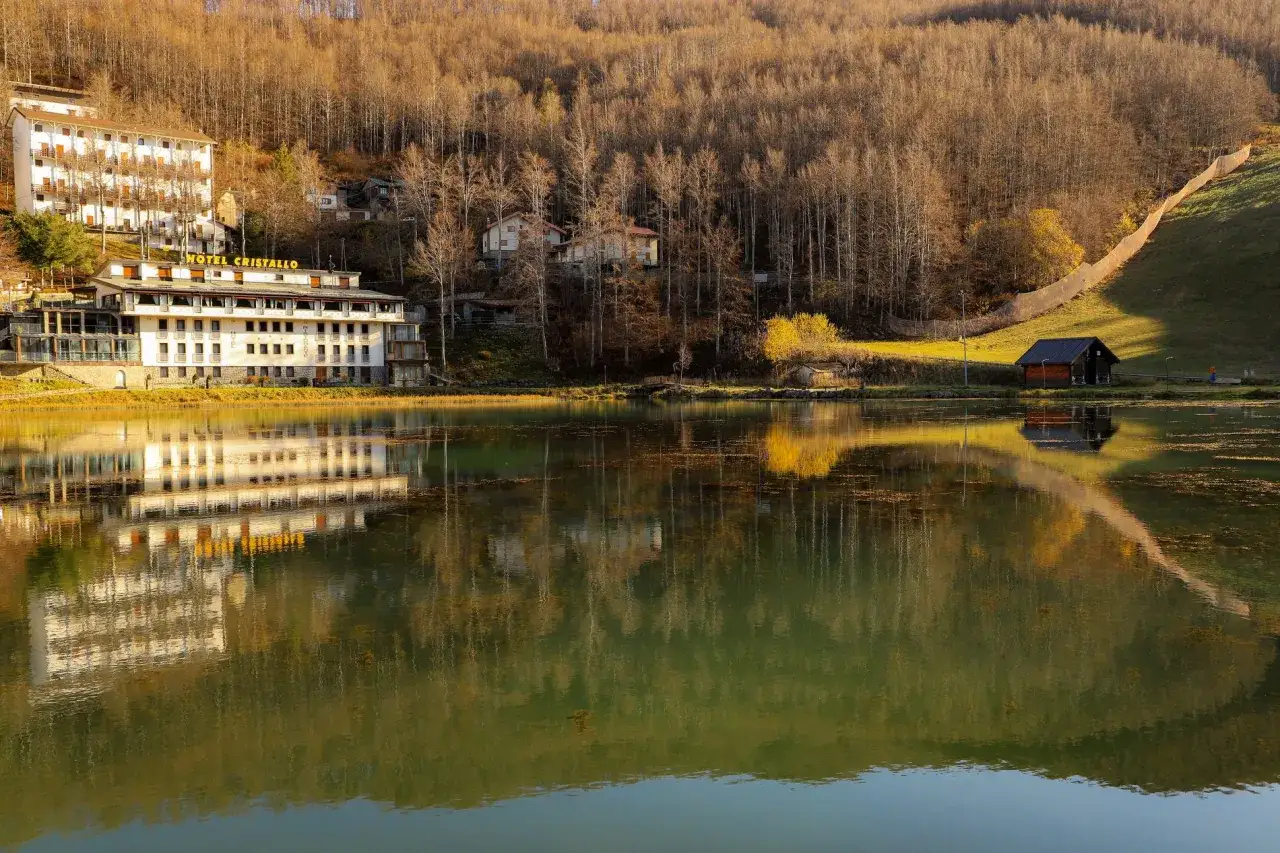 Hotel Cristallo sul Passo del Cerreto, riflesso sull'acqua calma del lago, circondato da boschi autunnali.
