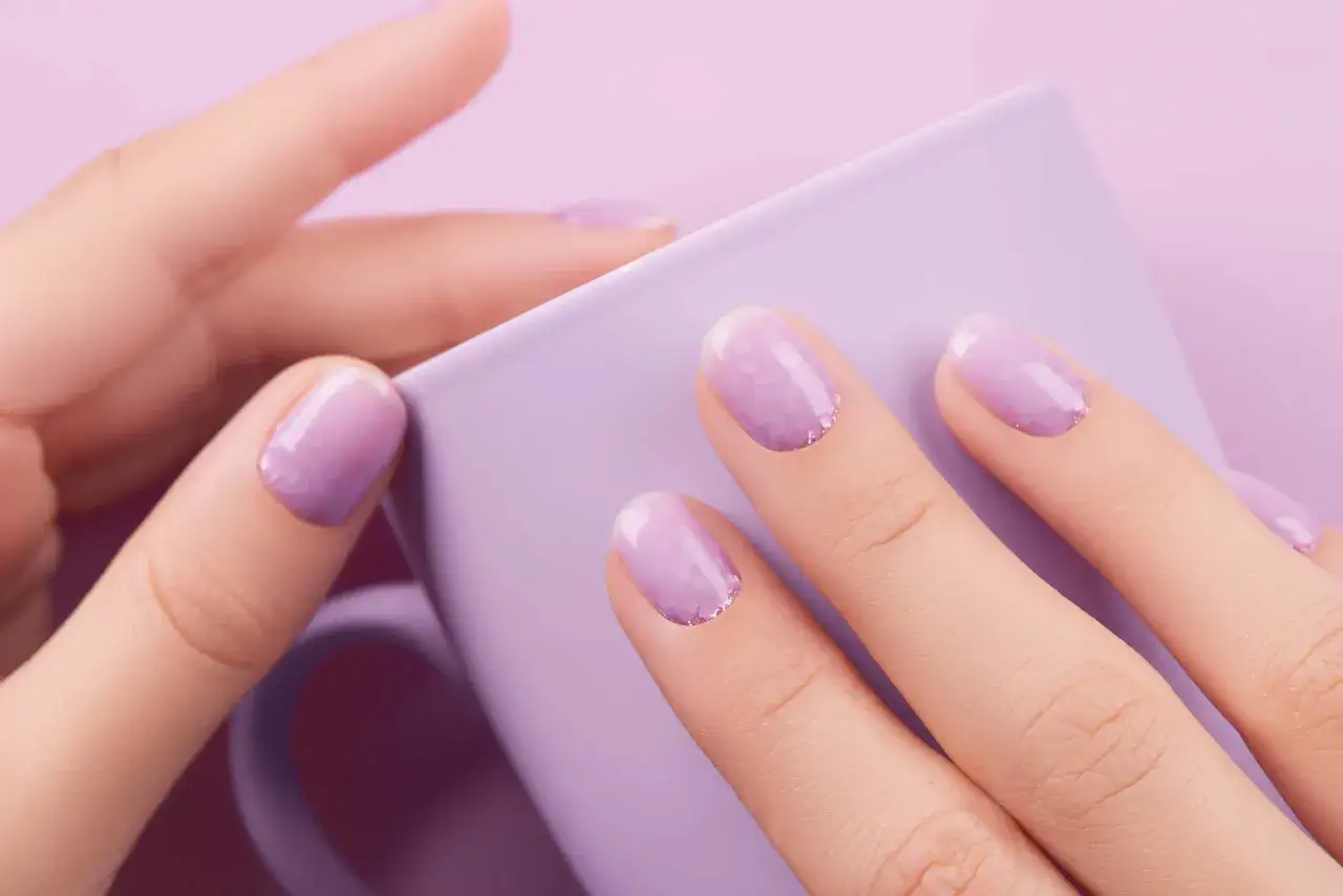 Mains d&eacute;licates aux ongles lavande paillet&eacute;s, tenant une tasse assortie. Un style baby boomer couleur, doux et tendance.