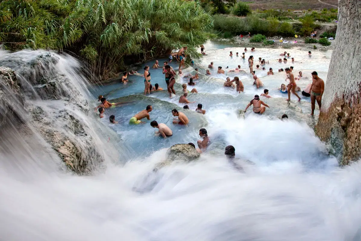 Cascate naturali con persone che si bagnano. Per raggiungere le terme di Saturnia, segui le indicazioni per il borgo.