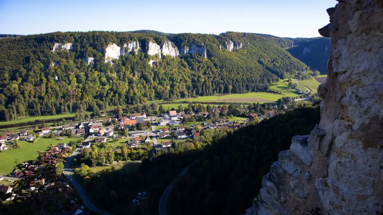 Blick von der ruine kallenberg auf ein malerisches Dorf im Tal, umgeben von bewaldeten Hängen und Felsformationen.