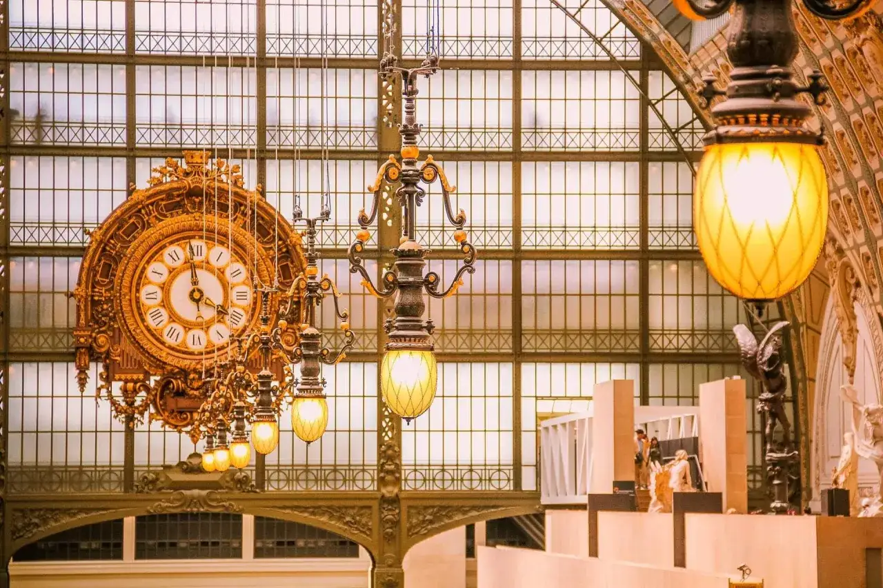 Złoty zegar i ozdobne lampy w muzeum d'Orsay. W tle przeszklony dach i fragmenty rzeźb.