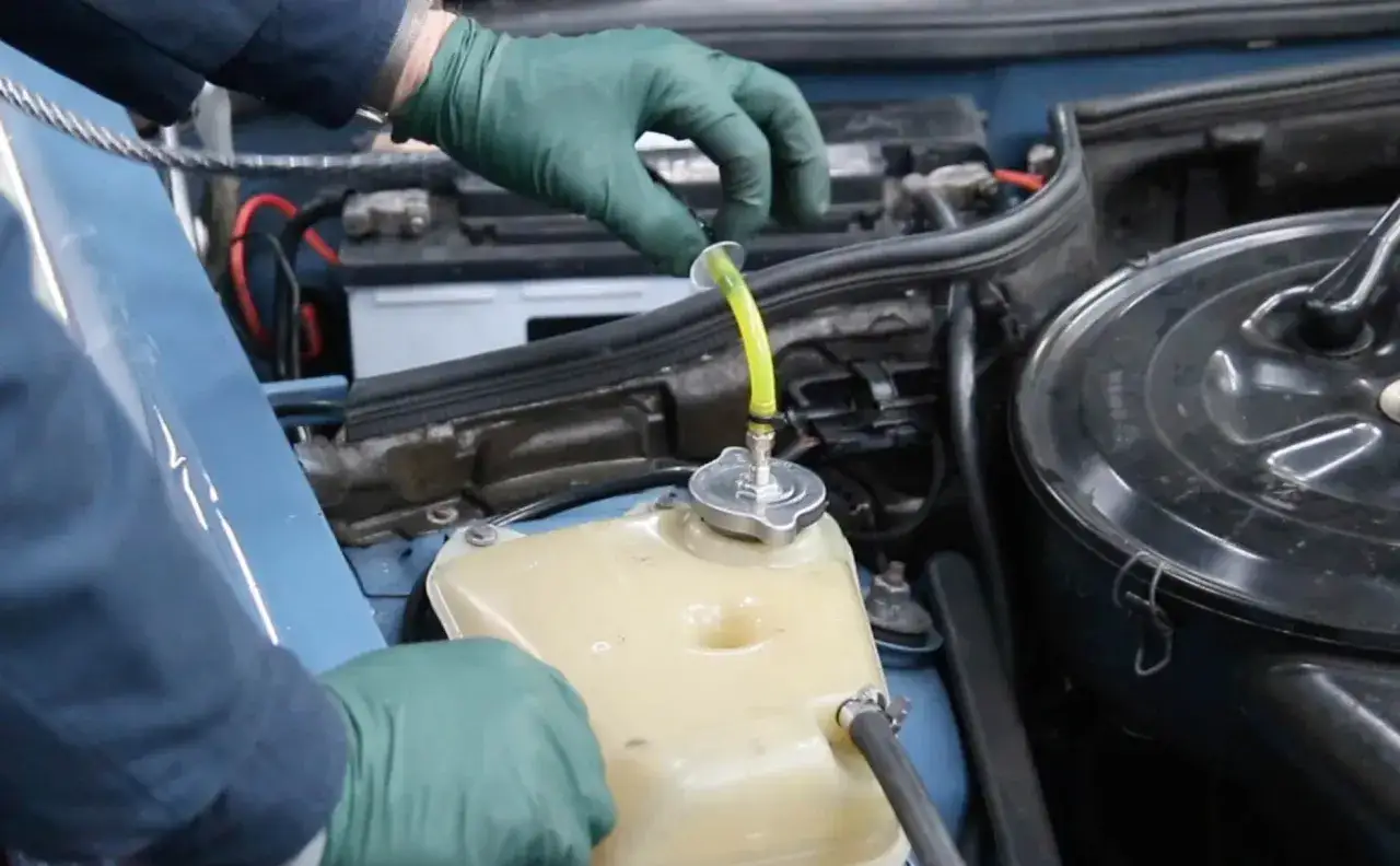 Mani con guanti verdi che aggiungono liquido giallo al serbatoio del radiatore, forse per risolvere una perdita liquido radiatore.