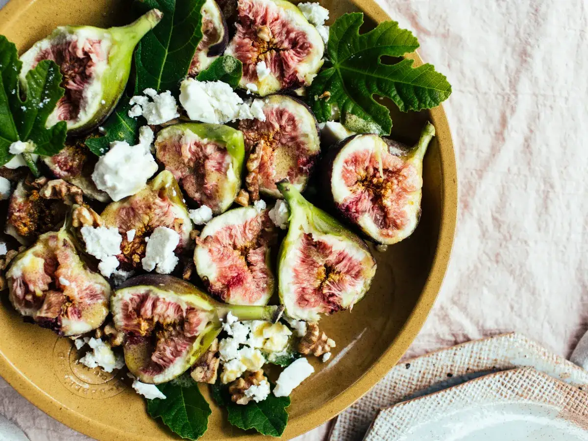 Ein köstlicher Feigensalat mit Feta, Walnüssen und frischen Feigenblättern auf einem rustikalen Teller.