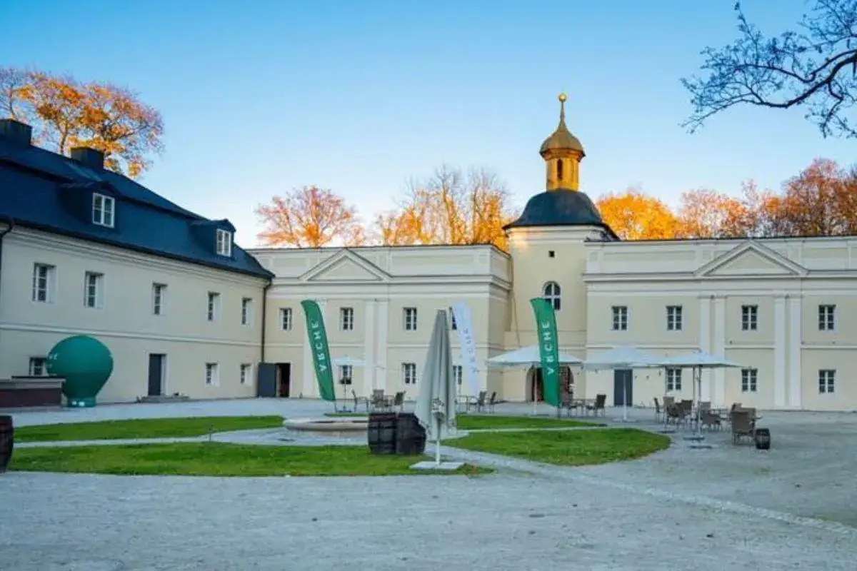 Pałac w Siemianowicach Śląskich z wieżą i złotą kopułą, otoczony zielenią i parasolami.