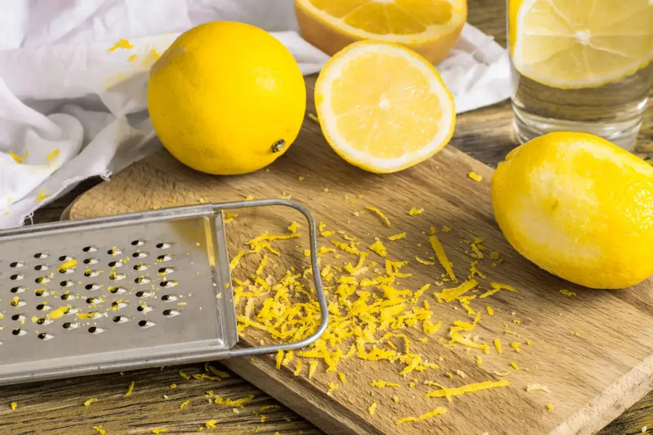 Un râpe et des citrons frais sur une planche en bois, avec du zeste de citron éparpillé.
