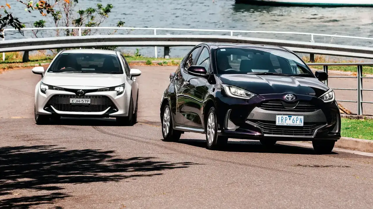 Dwa modele toyota hatchback: biały i ciemnofioletowy, jadące po drodze nad wodą.