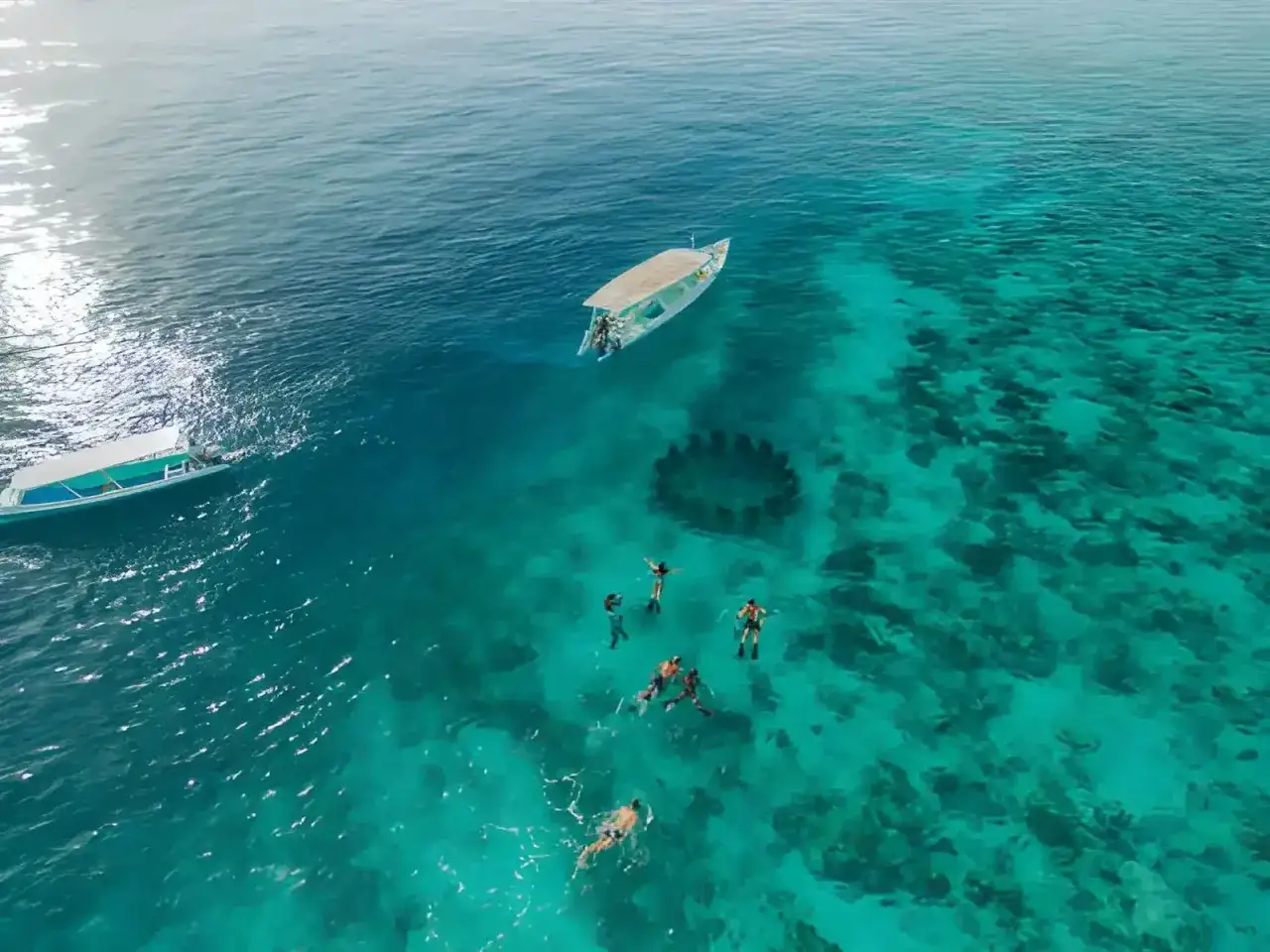Ludzie pływają w krystalicznie czystej wodzie obok łodzi, odkrywając podwodny świat. Idealne **bali w lipcu** na snorkeling.