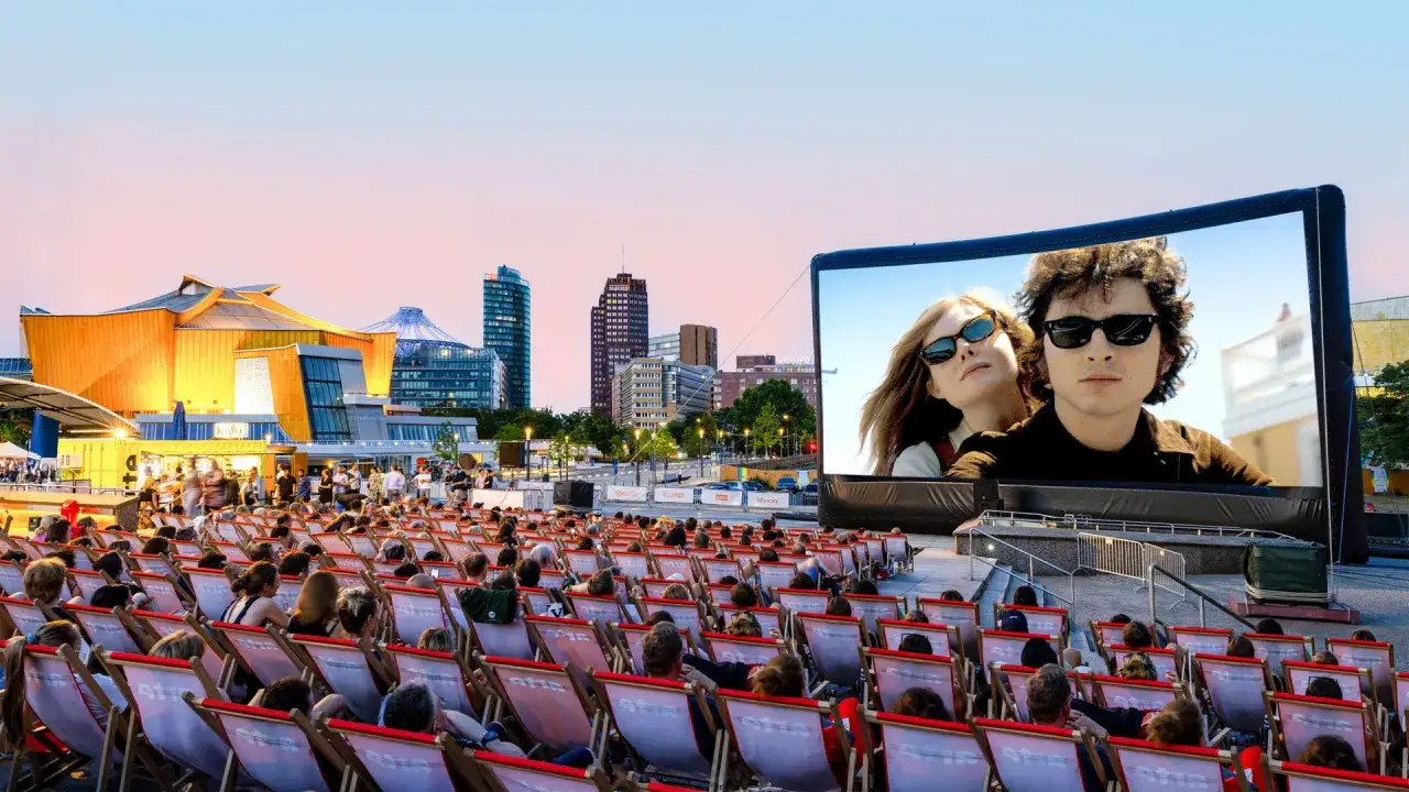 Ein Sommerabend im **Freiluftkino Charlottenburg**: Menschen sitzen in Liegest&uuml;hlen, vor ihnen eine riesige Leinwand mit einem Film, im Hintergrund die Berliner Skyline.