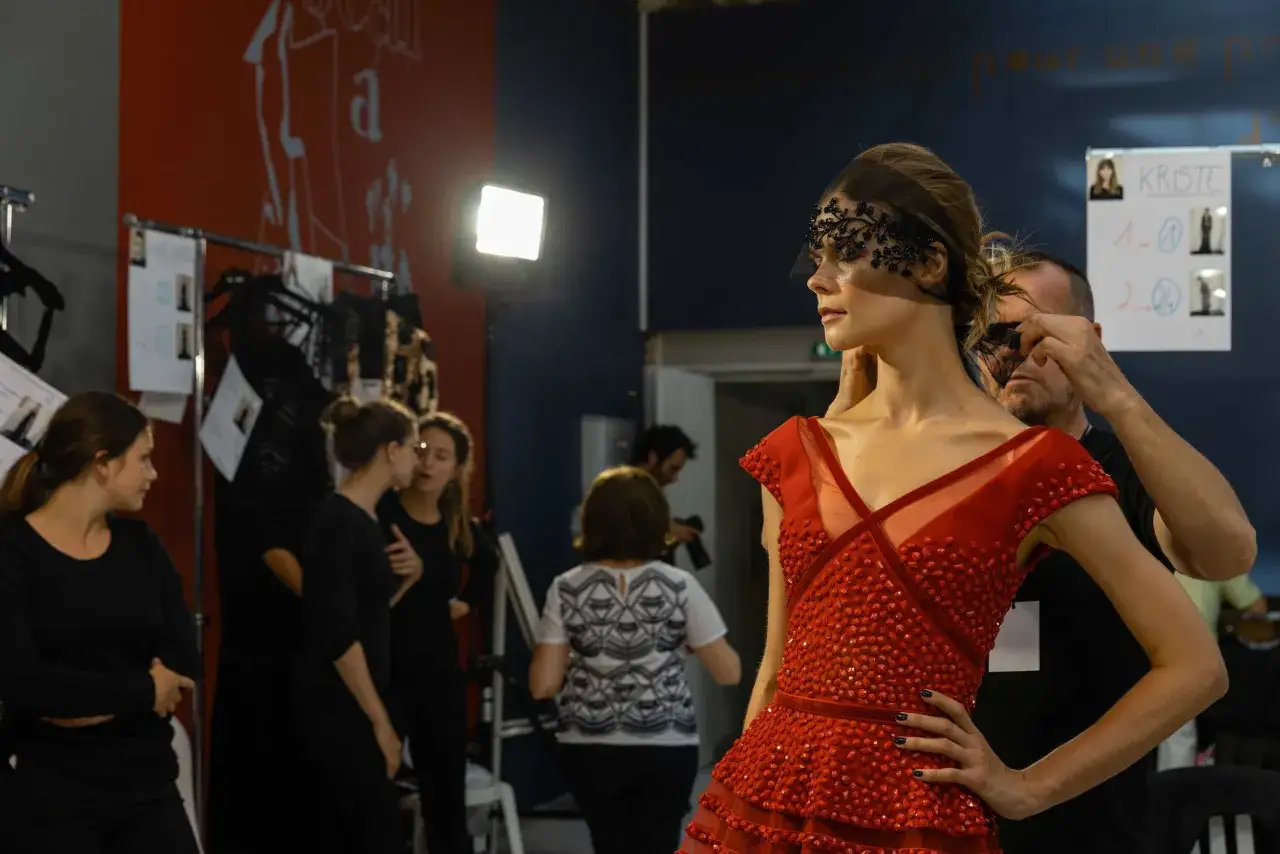 Dietro le quinte, Stefano Guindani cattura la modella con un abito rosso e un velo decorato.