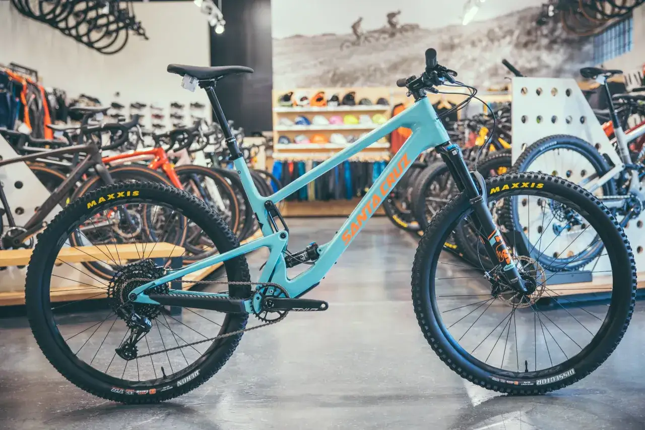 A teal Santa Cruz Tallboy 4 mountain bike with orange lettering sits in a bike shop, ready for adventure.