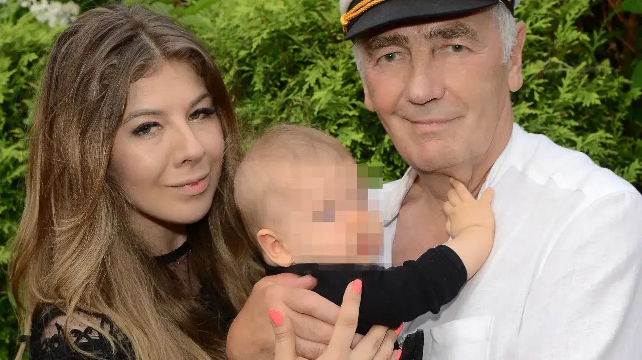 Karol Strasburger z żoną i dzieckiem. Uśmiechnięty mężczyzna w kapeluszu trzyma na rękach niemowlę, obok stoi młoda kobieta.