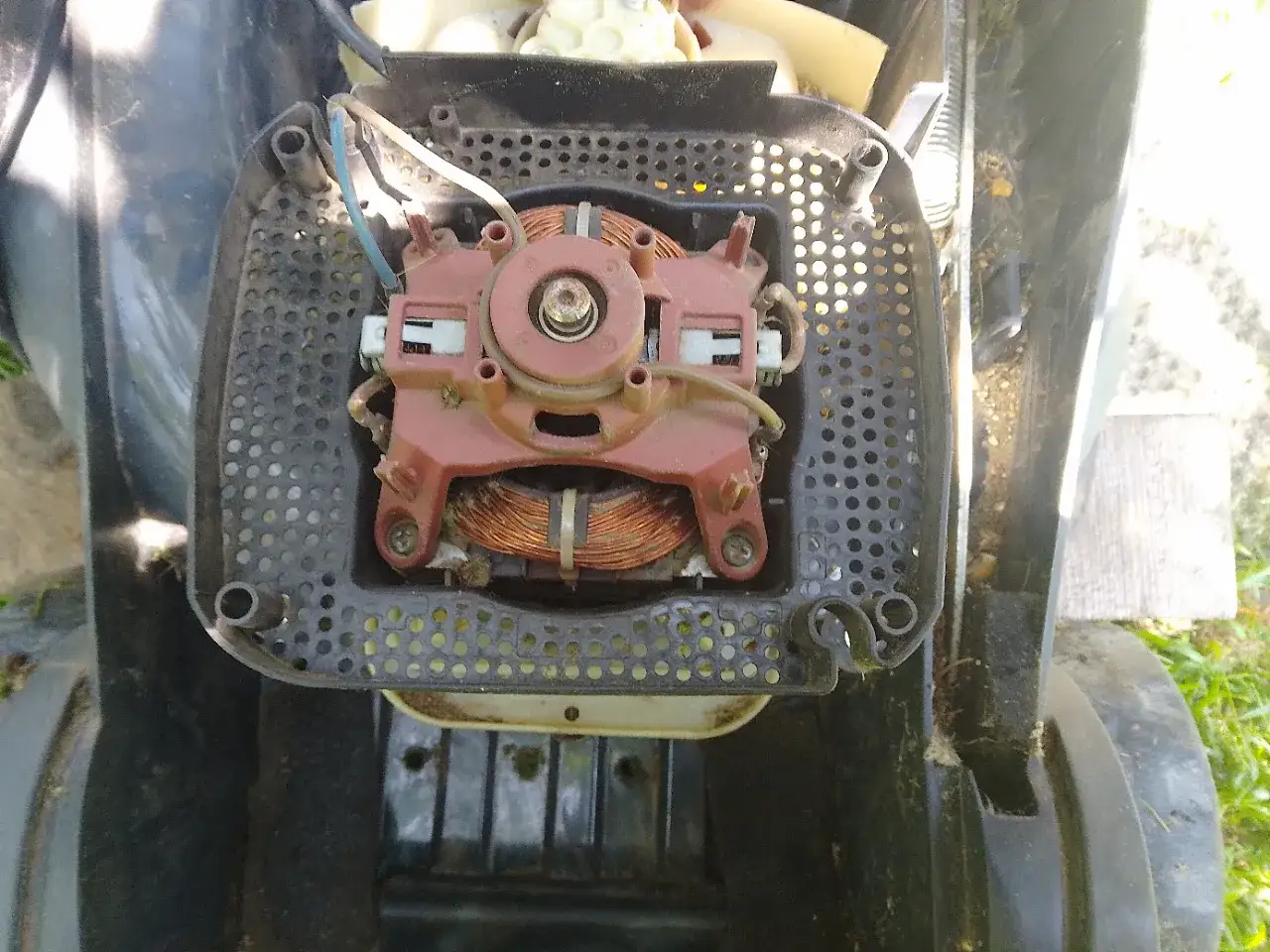 Widok z góry na silnik elektryczny do kosiarki z miedzianymi uzwojeniami, częściowo zakryty czarną obudową z otworami.