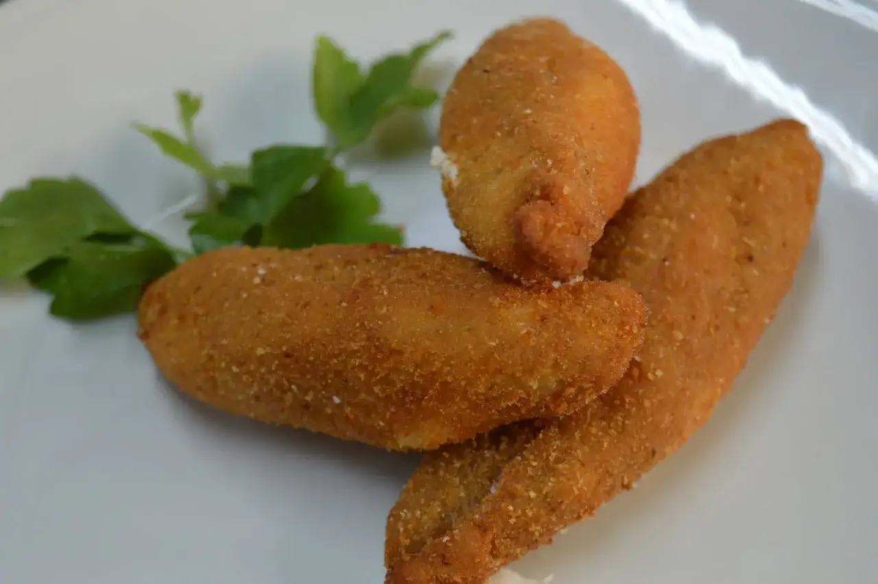 Fiori di zucca in padella, dorati e croccanti, serviti su un piatto bianco con un rametto di prezzemolo.