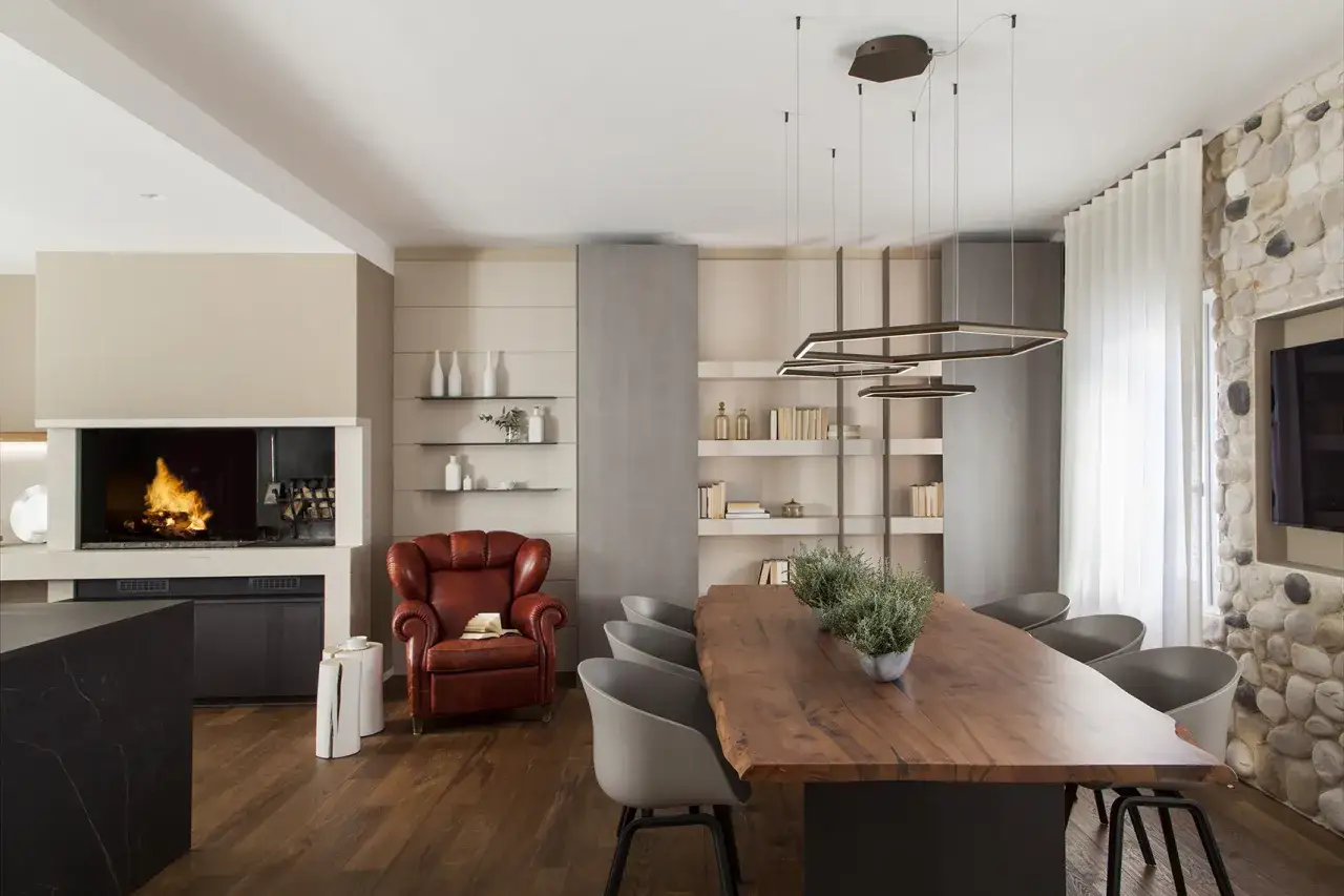 Un accogliente soggiorno con camino acceso, poltrona in pelle e un tavolo da pranzo in legno massello. Un esempio di design interni moderno e caldo.