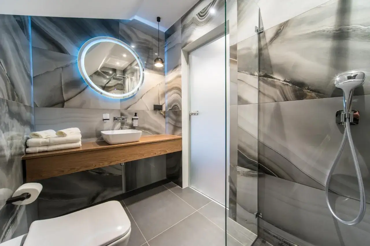 Nowoczesna łazienka w hotelu kameralnym Zielona Góra. Marmurowe płytki, podświetlane lustro i drewniana szafka tworzą elegancką przestrzeń.