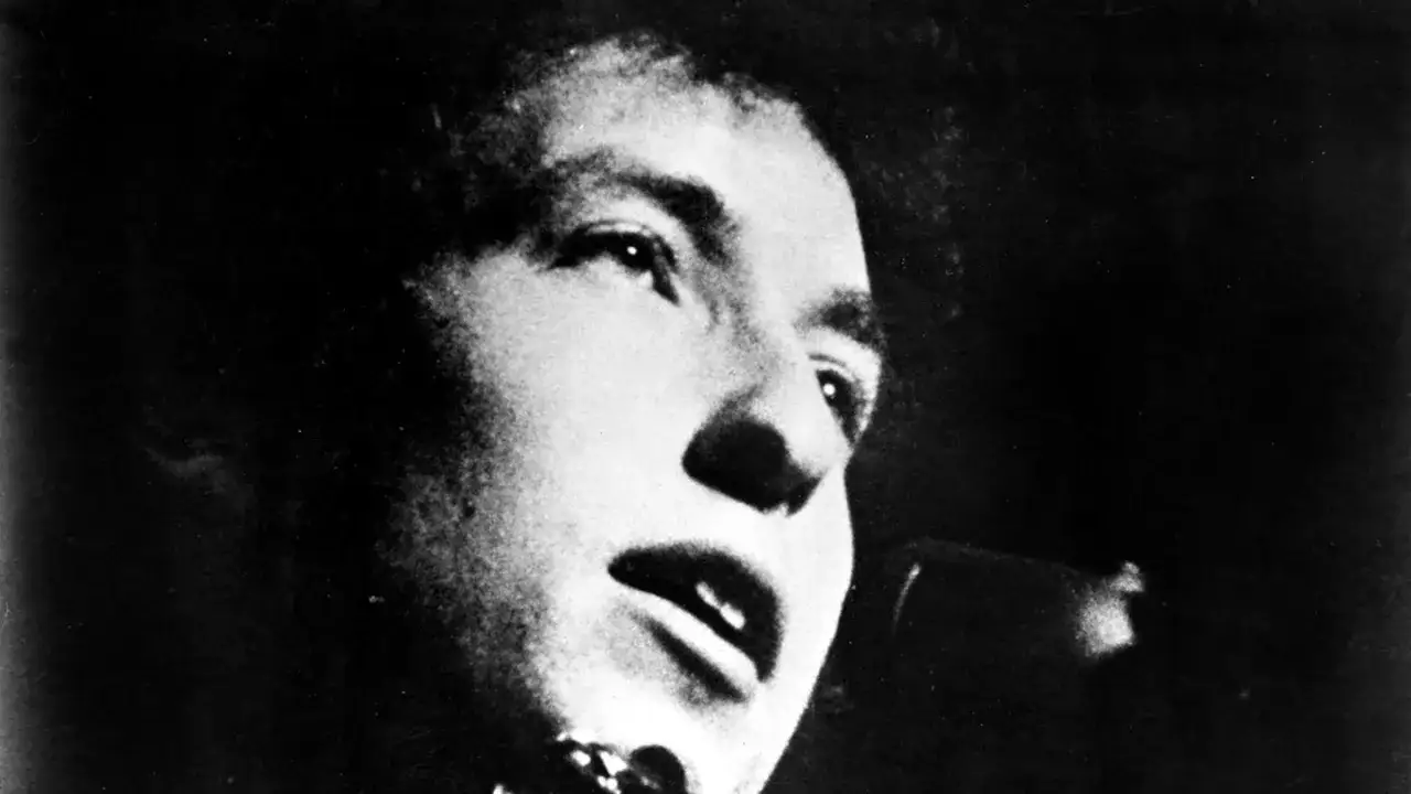 Närbild på Bob Dylan i en svartvit film, med blicken riktad uppåt och munnen öppen som om han sjunger.