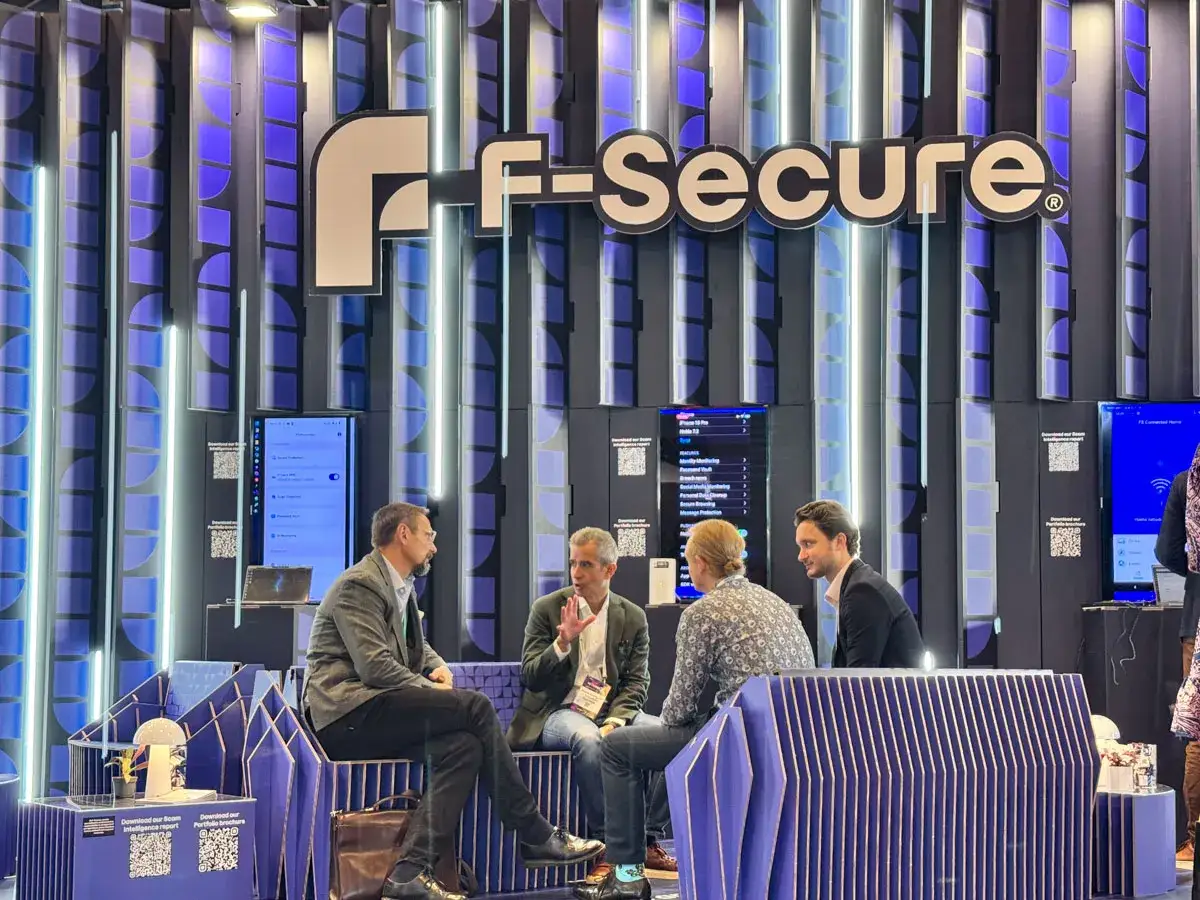 Hombres conversan en un stand de F-Secure durante una feria empresarial.