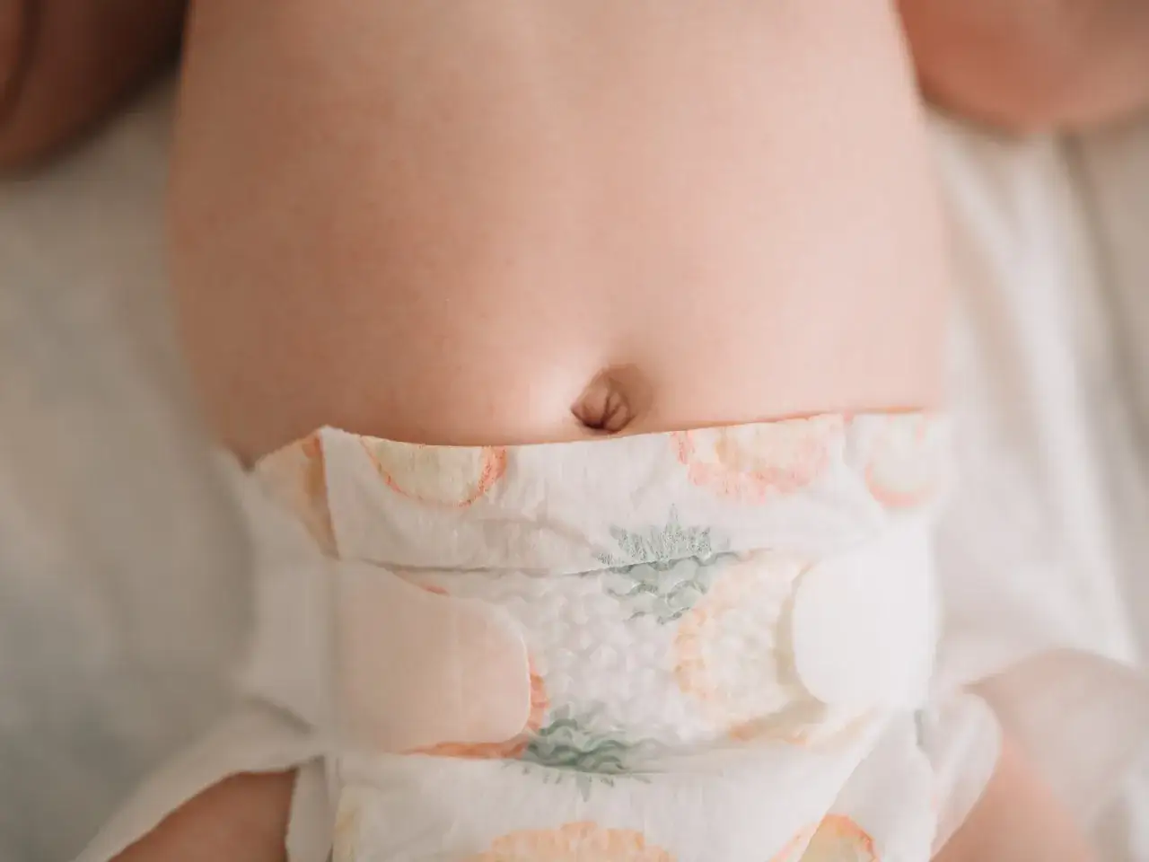 Babybauch mit Nabel, an dem die Nabelschnur abgefallen ist und eine leichte Kruste bildet.