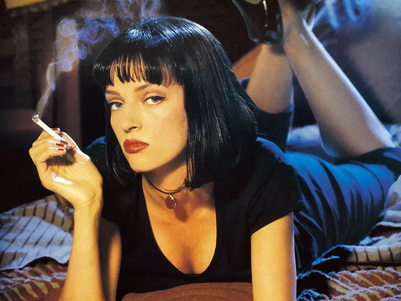 Uma Thurman w kultowej scenie z filmów. Pali papierosa, leżąc na łóżku.